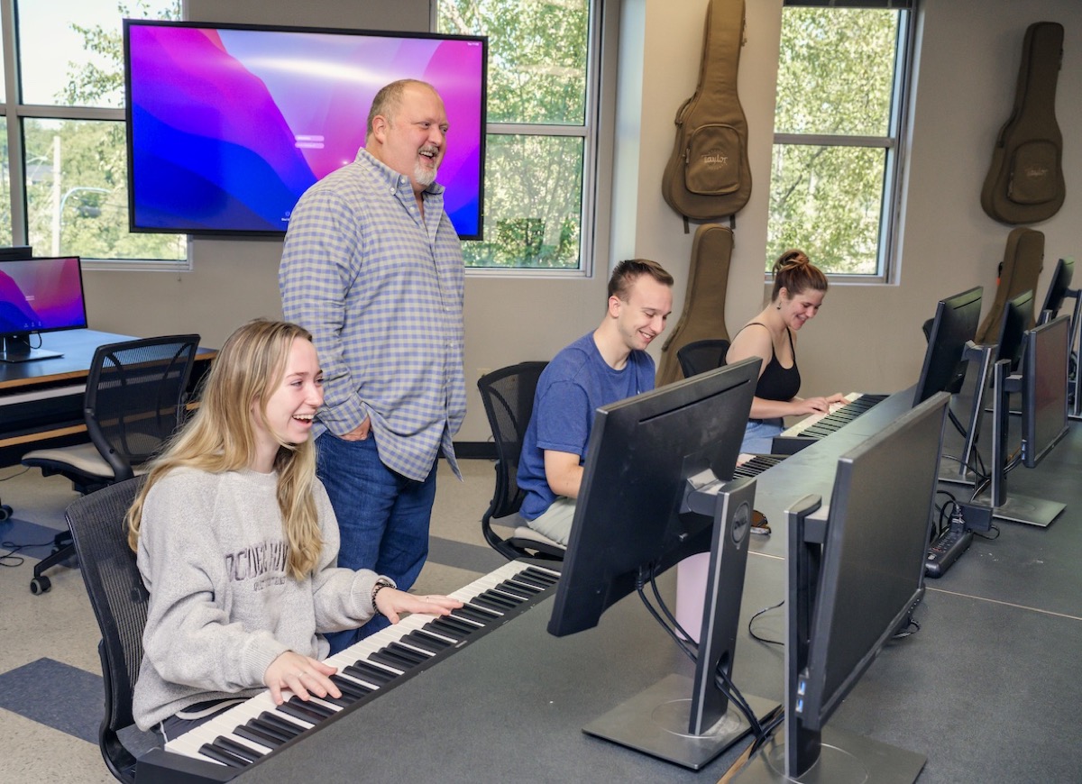 Odie Blackmon standing in the MTSU songwriting lab while students work at keyboards.
